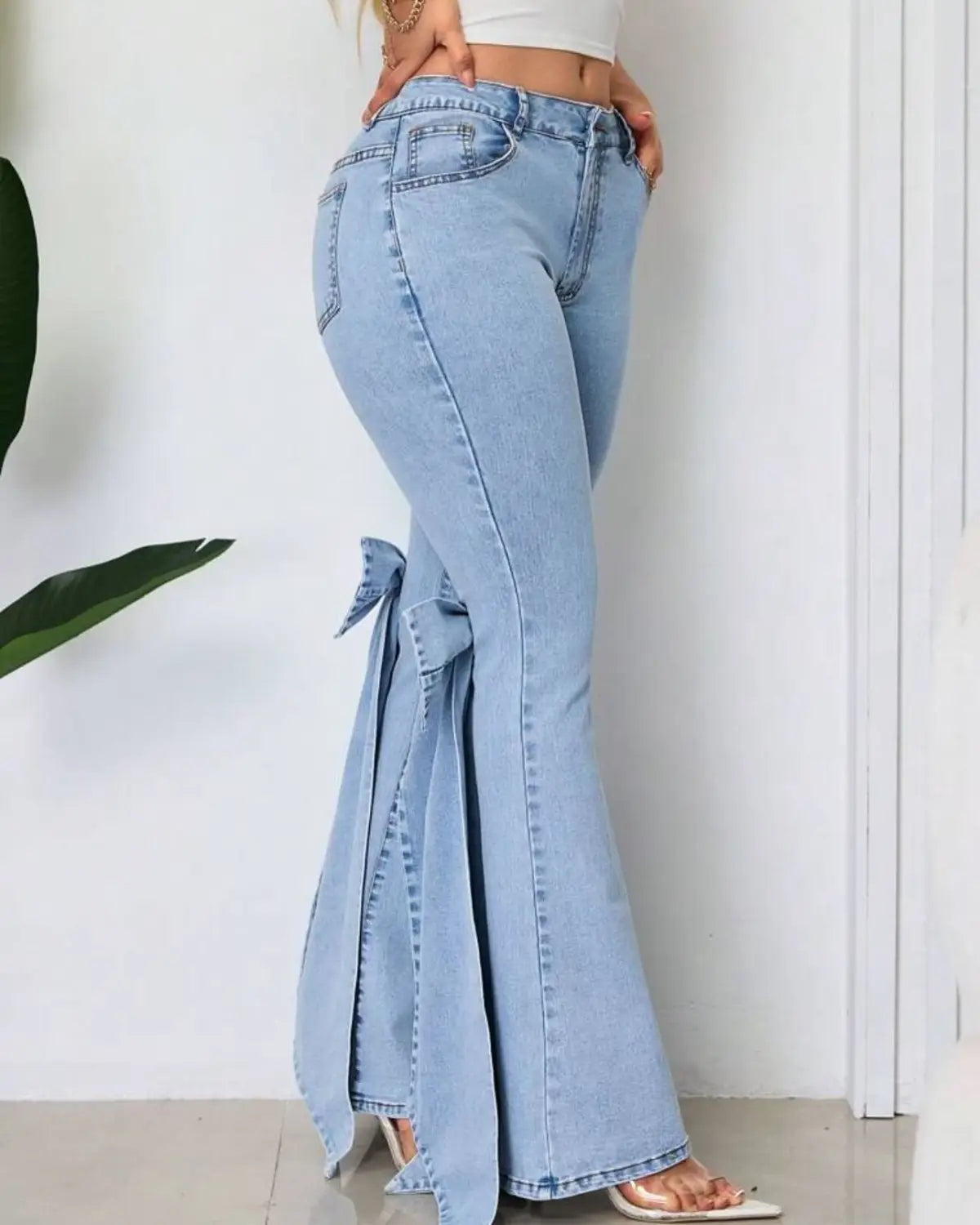 Jean évasé taille haute en denim délavé clair avec un détail de nœud décoratif à la cheville.