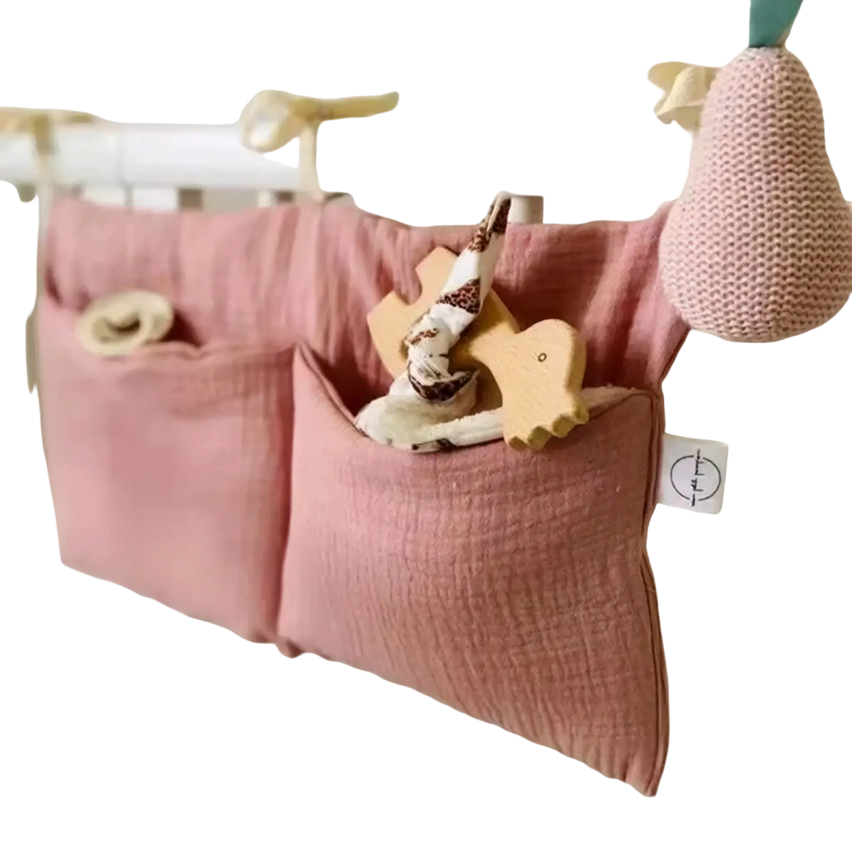 Pink cotton baby crib storage bag with two pockets hanging on white crib rail for bedside organization