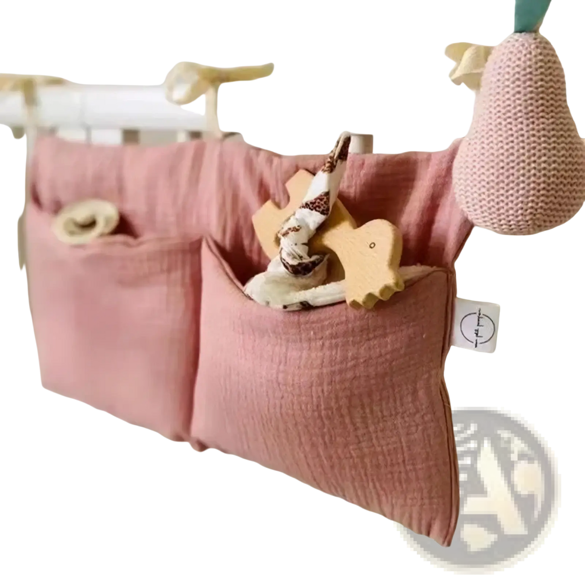 Pink cotton baby crib storage bag with two pockets hanging on white crib rail for bedside organization