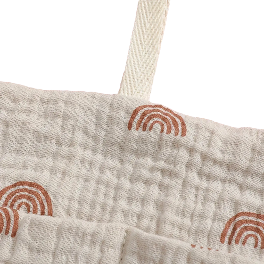 Baby crib storage bag cotton bedside organizer in off-white gauze fabric with textured weave and small brown rainbow prints