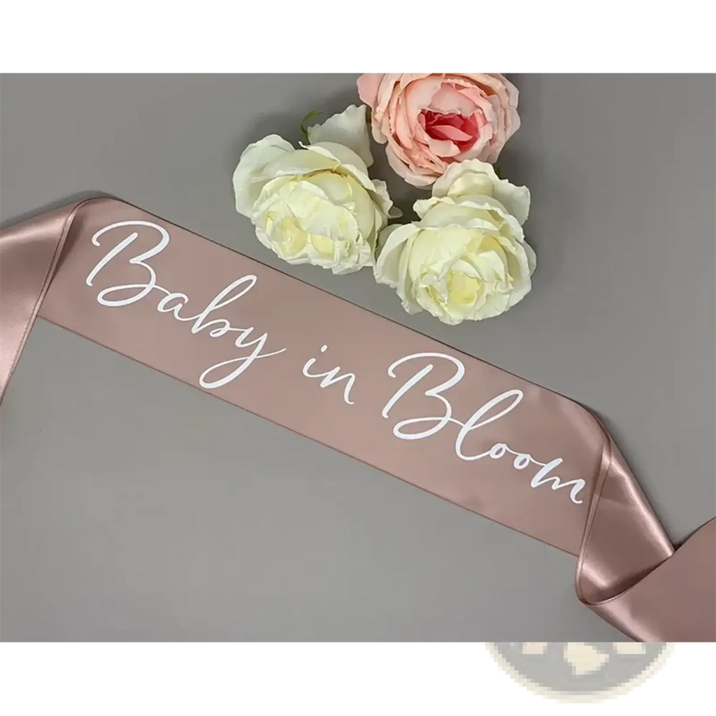 A rose gold satin baby shower sash with white cursive baby in bloom text for mum to be maternity wear