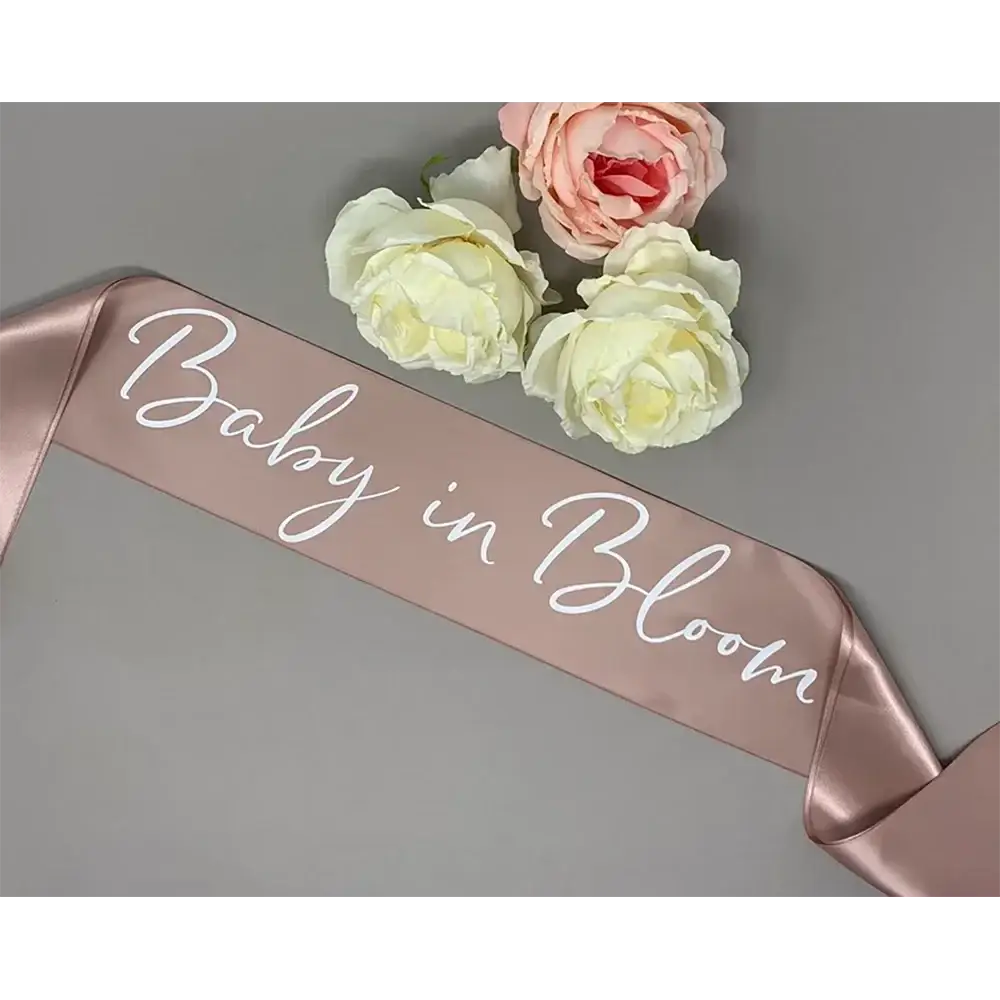 A rose gold satin baby shower sash with white cursive baby in bloom text for mum to be maternity wear