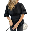 Black cotton peplum top with puffed sleeves and cinched waistband shown from the back with tie back detail