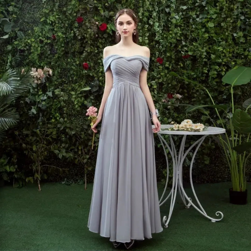 A flowing off-the-shoulder gray chiffon floor length bridesmaid gown with a fitted bodice and full skirt.