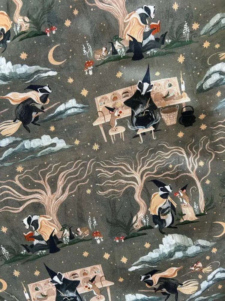 Dark gray cotton dress fabric featuring whimsical badgers in wizard attire reading books and flying on brooms