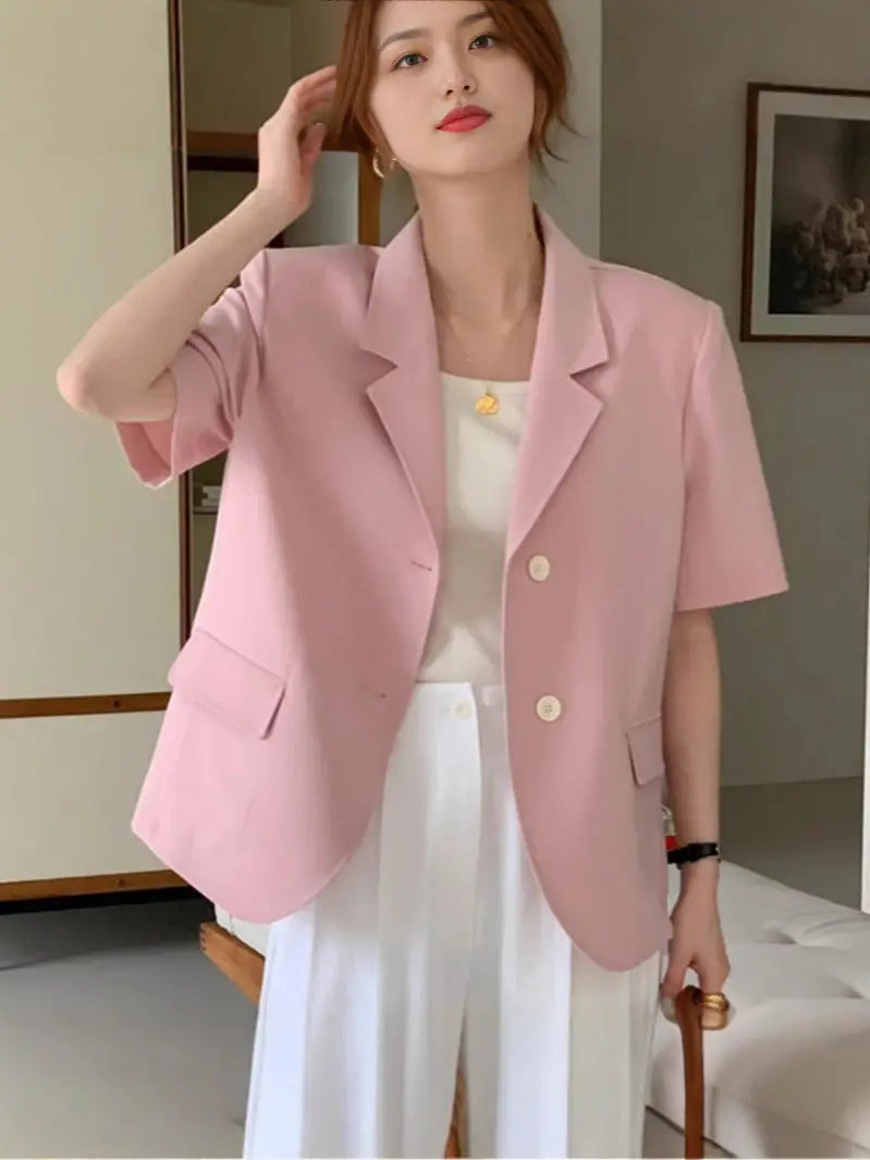 女性向けの柔らかなピンクの半袖ブレザーで、クラシックカラーと前面のボタン2つを備え、リラックスフィットのカジュアルジャケットとして設計されています。
