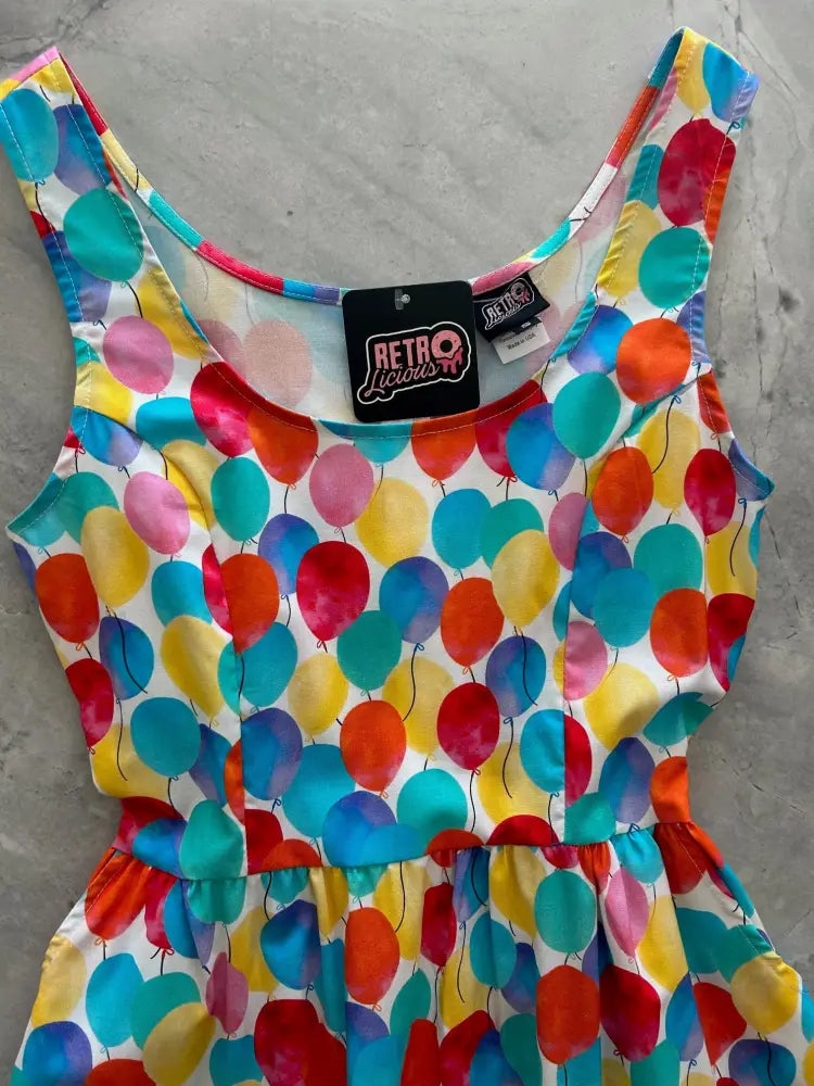 A vibrant sleeveless fit and flare dress with a watercolor balloon print in red blue yellow and pink on white background