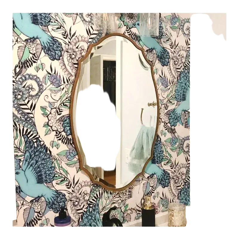 An oval bathroom mirror with a gold ornate frame hangs on blue and black bird and flower wallpaper