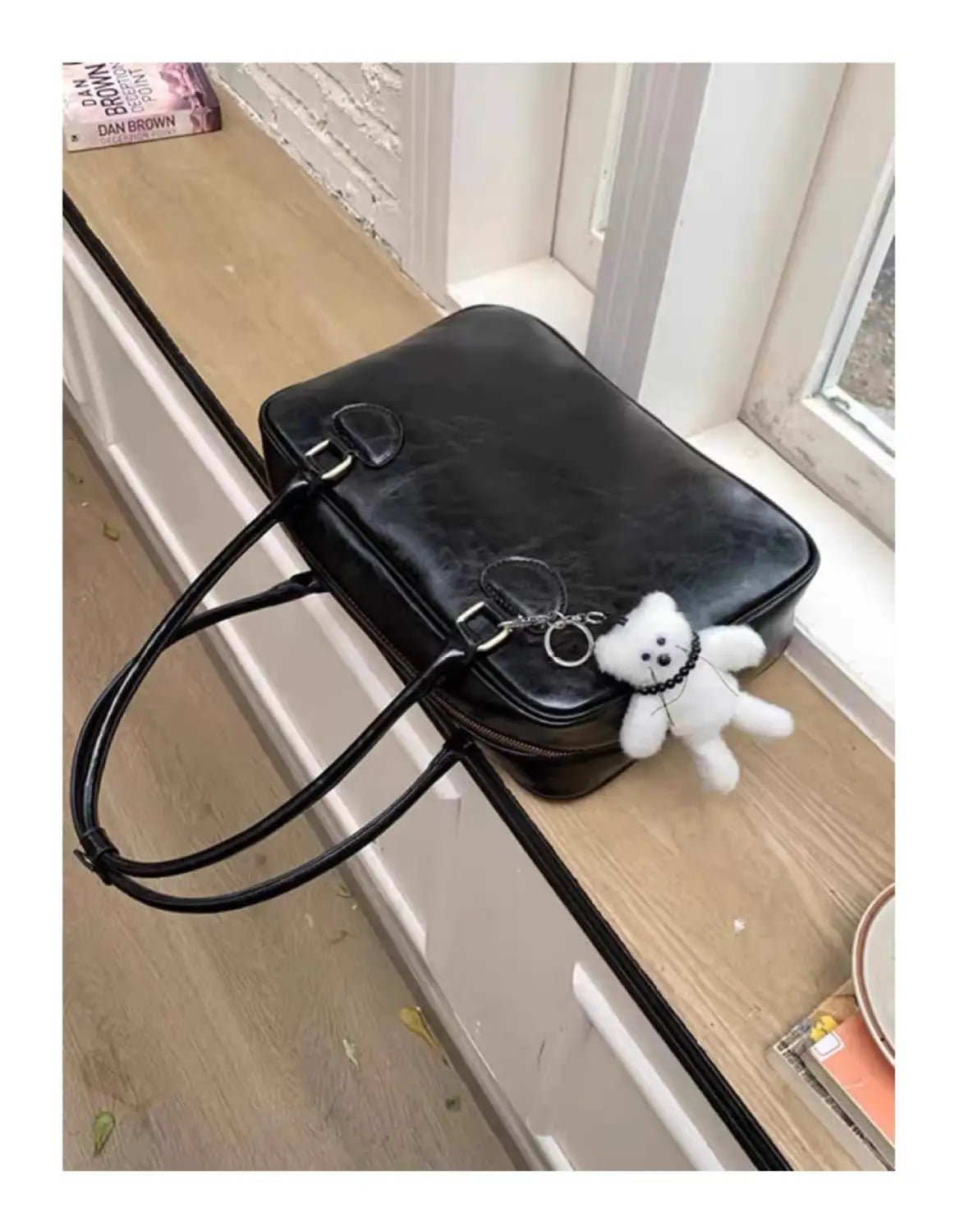 Black leather large capacity shoulder bag with long handles and a white teddy bear keychain attached to the front zipper pull.