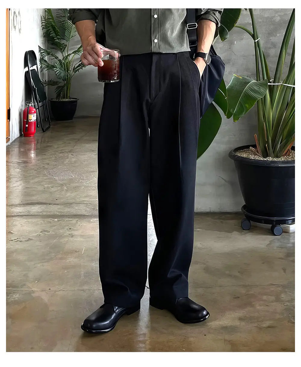 Pantalones de vestir anchos plisados color gris oscuro para hombre con un corte a medida y pliegues sutiles.