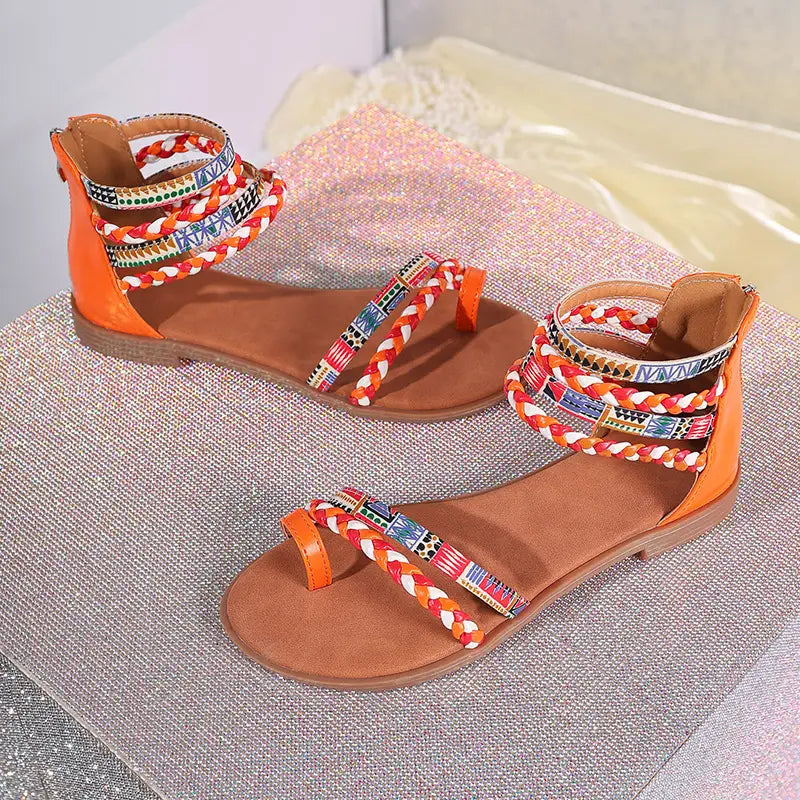 Vibrant orange and brown bohemian ethnic flat sandals featuring colorful braided ankle straps and strappy design.