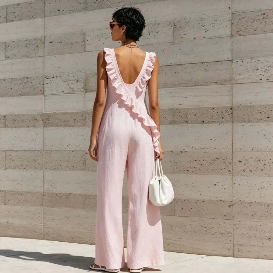 A soft pink sleeveless ruffled v-neck resort jumpsuit showing the back side with detailed ruffle design.