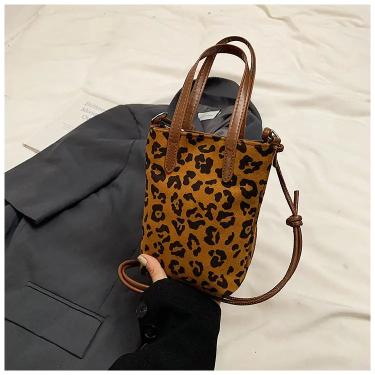 Retro leopard print suede mini bucket crossbody bag in tan and black with brown leather handles and an adjustable strap.
