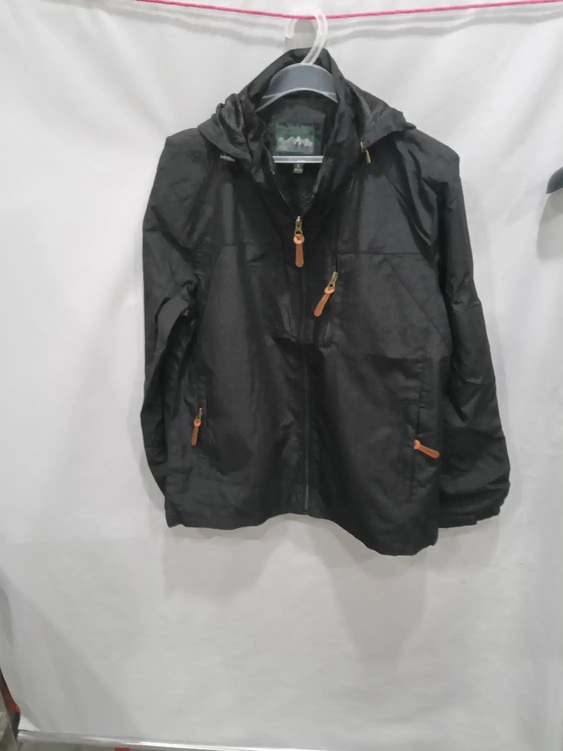 Chaqueta de senderismo con capucha impermeable color negro, con tiradores de cremallera color camel y una etiqueta de marca sutil en el cuello