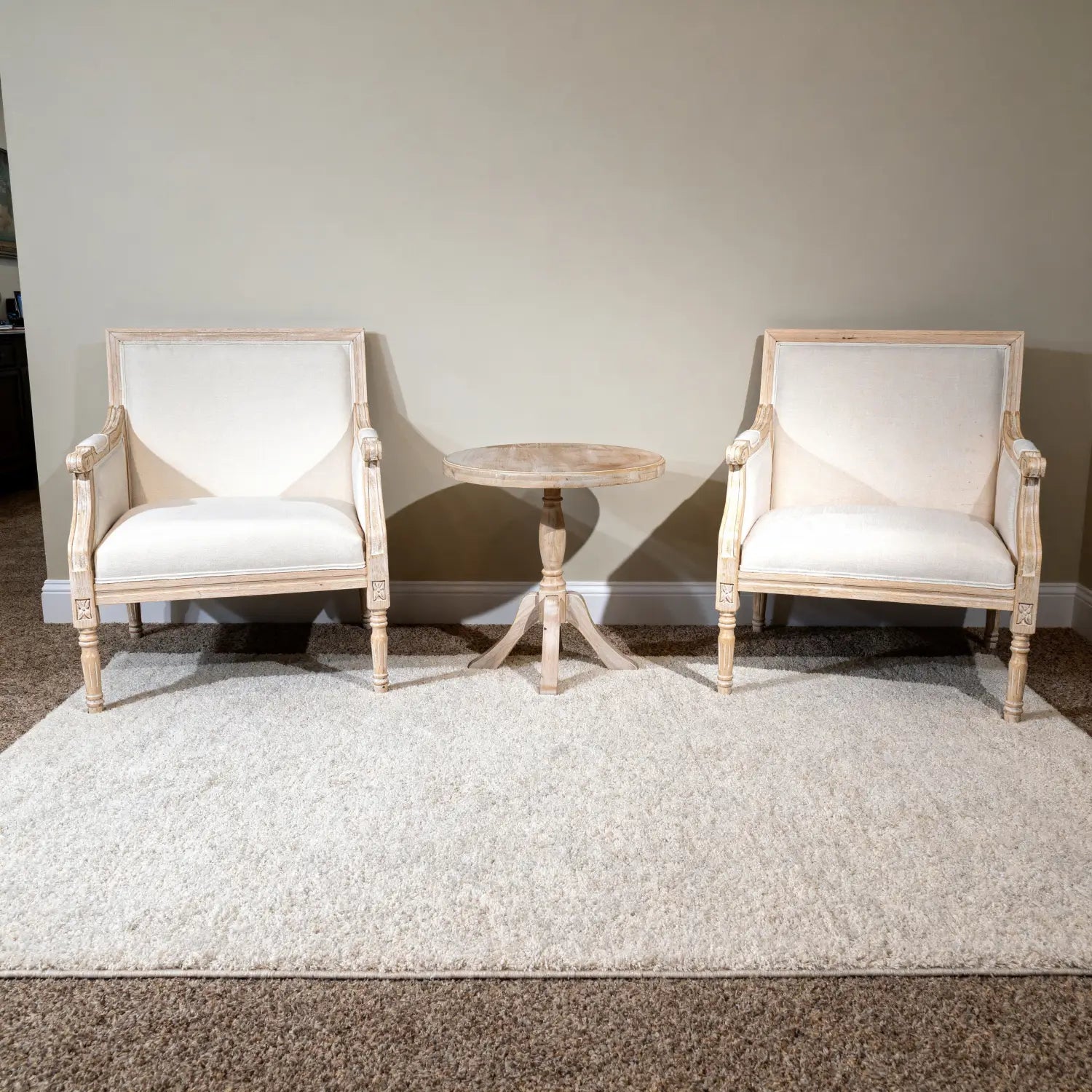 Par de sillas francesas de acento color crema, tapizadas en lino, con marcos de madera clara envejecida y tallados ornamentales.