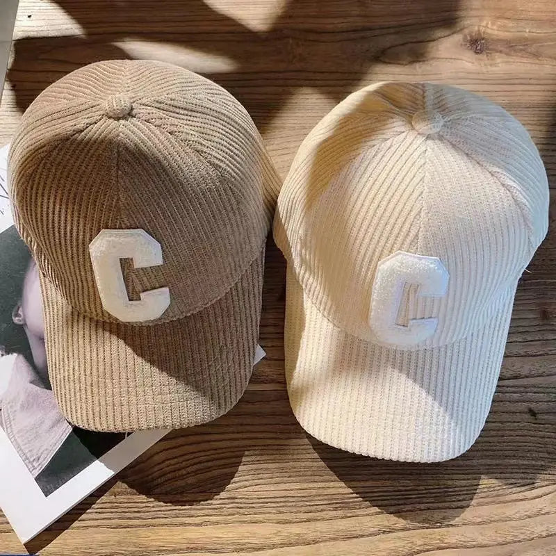 two corduroy baseball caps in beige and off-white featuring a prominent white embroidered letter c on the front.