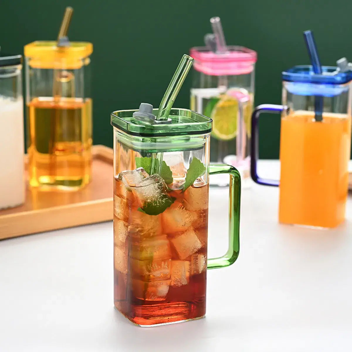 Tasse carrée en verre avec couvercle et paille de 12 oz, carafe en verre teinté vert avec couvercle et poignée assortis, remplie de thé glacé et de feuilles de menthe.
