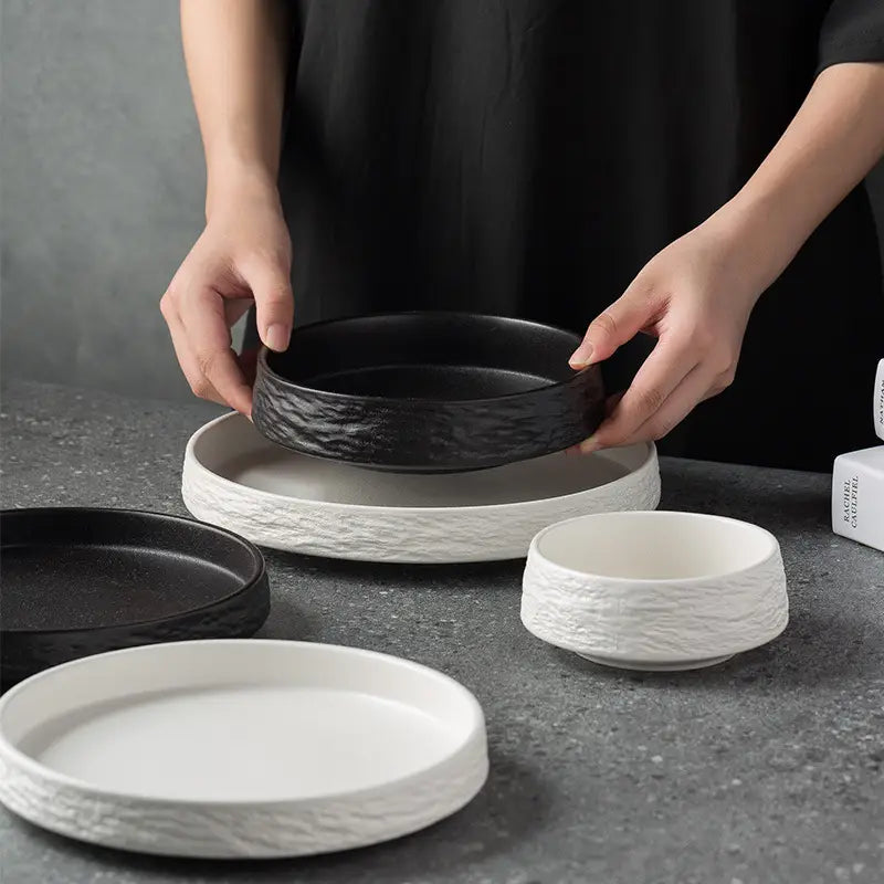 Cuenco de cerámica negra con superficie rústica texturizada sostenido por encima de un plato a juego de cerámica con patrón de piedra, conjunto de vajilla japonesa de plato hondo.