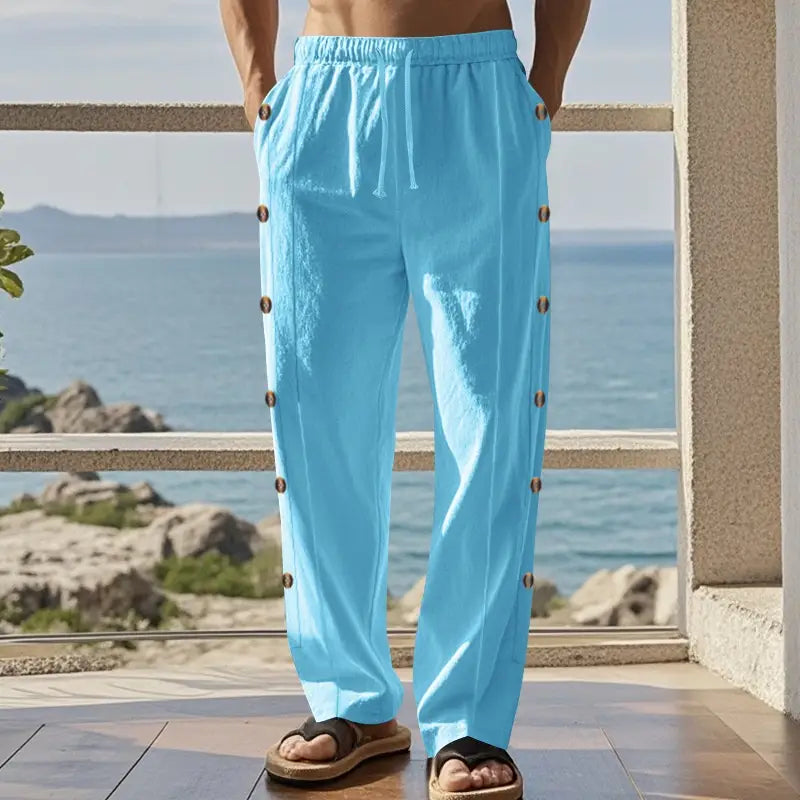Light blue men’s linen straight leg pants featuring a loose fit with a drawstring waist and decorative brown buttons running down each leg.