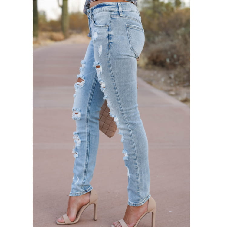 Pantalones vaqueros ajustados tipo skinny de mezclilla con efecto lavado claro desgastados con detalles de rotura a lo largo de las piernas.