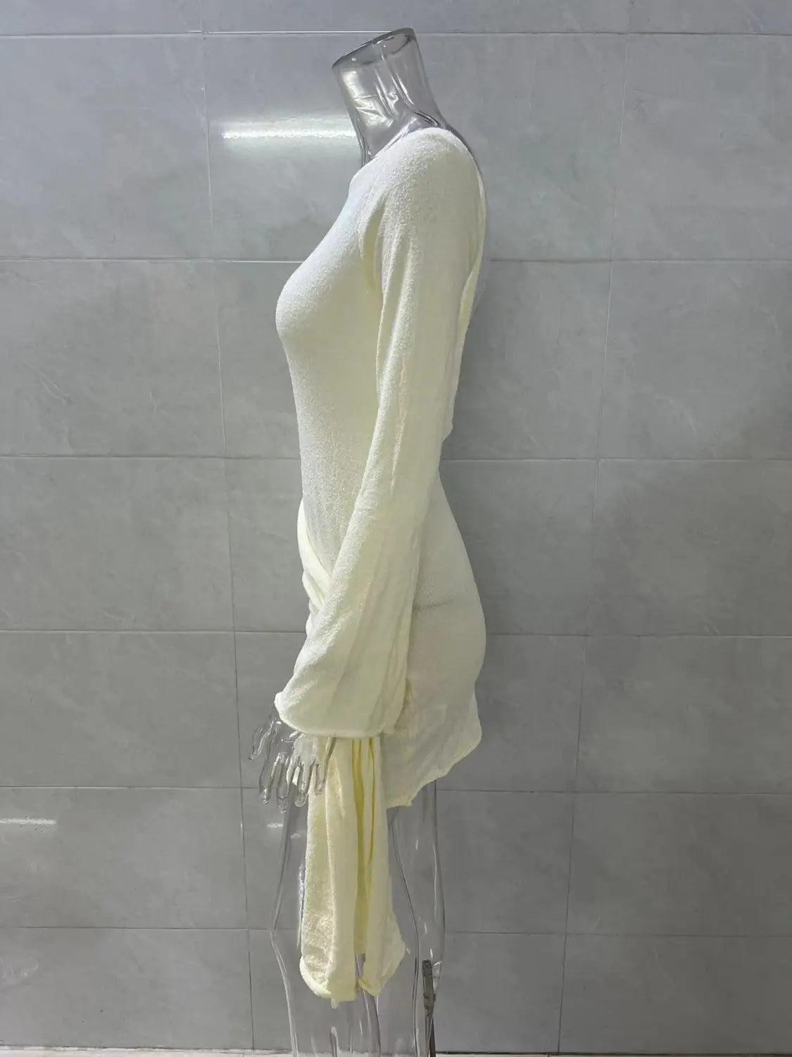 Backless long sleeve knit mini dress in cream color featuring a draped asymmetrical hemline and side tie detail.