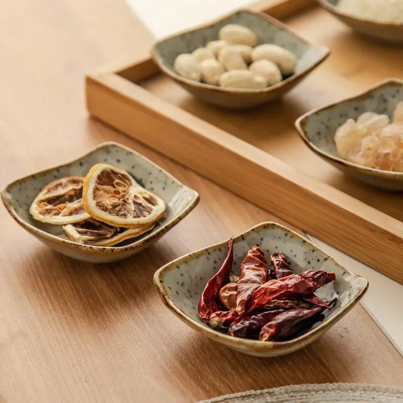 Square Japanese style ceramic sea creature sauce dish with speckled gray glaze and slightly raised rim holding dried citrus slices.