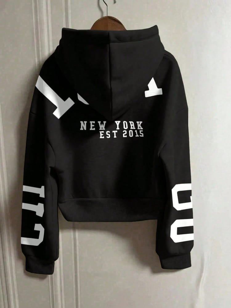 Sweat-shirt à capuche zippé imprimé graphique noir court, présentant le dos avec le texte « New York Est 2015 » blanc et des graphiques géométriques audacieux sur les manches et le dos.