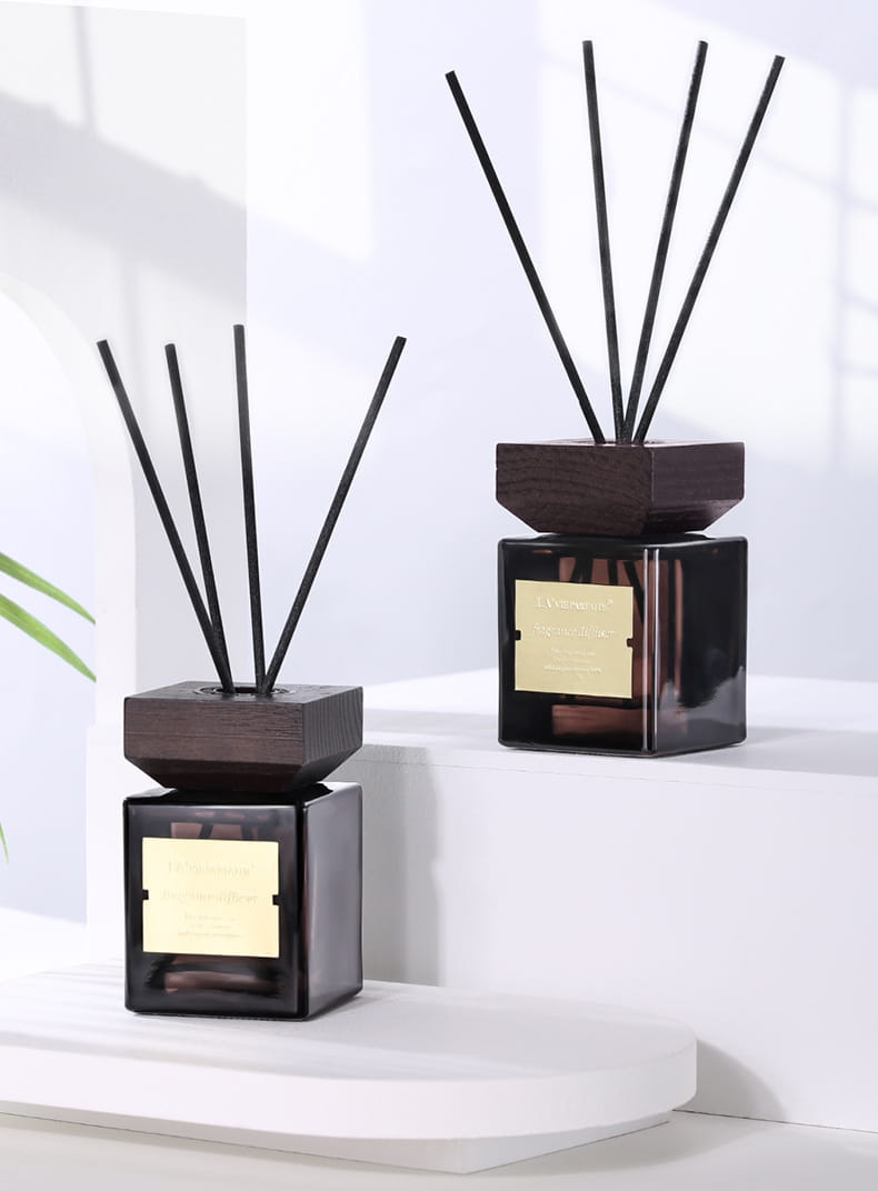 Diffuseurs à roseaux en verre noir élégants, avec dessus en bois foncé et plaques dorées, contenant de minces tiges de roseaux noirs pour une utilisation en parfum d’hôtel.