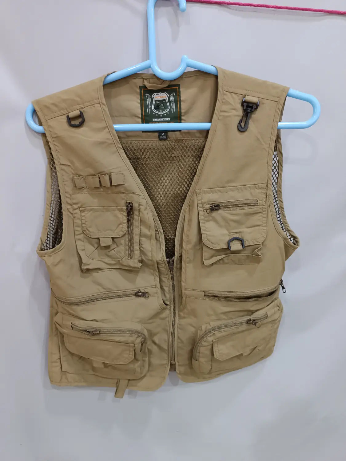 Tanfarbene taktische Wanderweste mit 14 Taschen, Mesh-Futter und einem Markenlabel am Kragen, ausgelegt für Cargo- und Outdoor-Einsatz.