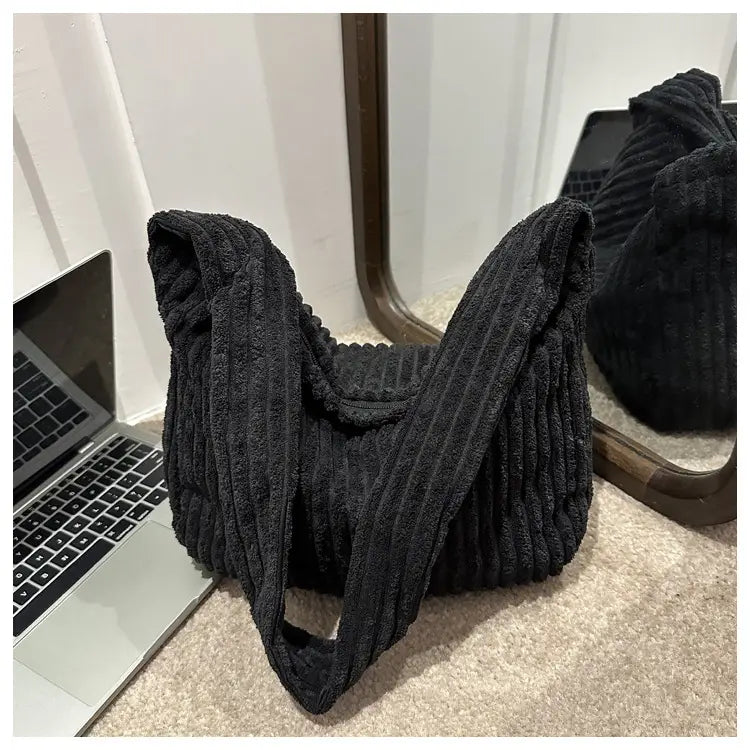 Schwarzer Corduroy-Schulterbeutel mit kräftiger gerippter Textur und breiten Trägern, ausgelegt für minimalistisches Streetwear.