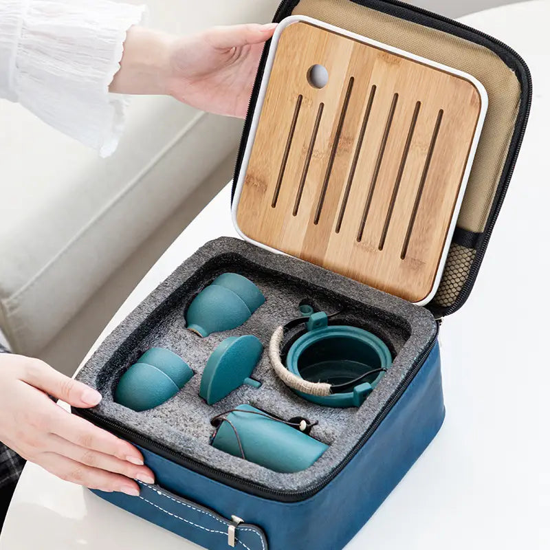 Teal ceramic travel tea set with bamboo tray nestled in a blue fabric carrying case.