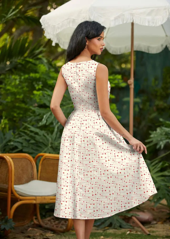 A woman wearing a sleeveless white cotton midi dress with subtle red geometric heart print from be mine