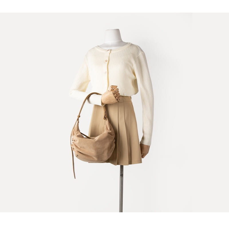 Beige suede dumpling shoulder bag with a long adjustable strap and front tie closure designed as a slouchy crossbody hobo.