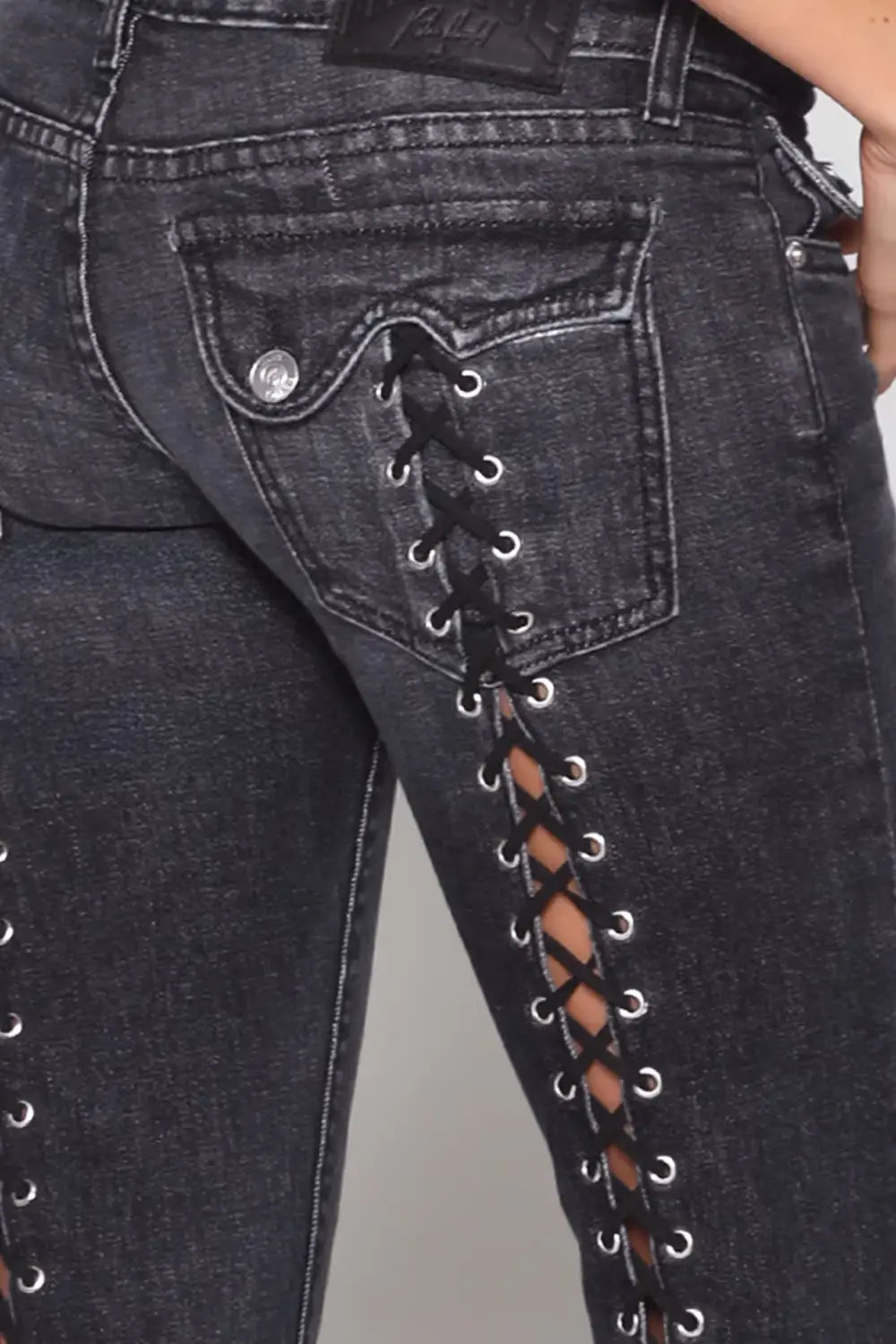 Jeans de mezclilla de tiro bajo tipo campana de lavado oscuro mostrados por la parte posterior, con un bolsillo trasero con cordones que presenta ojales de tono plateado y cordones negros.