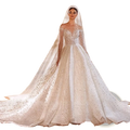 Beaded ball gown wedding dress with long sleeves featuring an off-the-shoulder white lace and embellished design with flowing train and veil