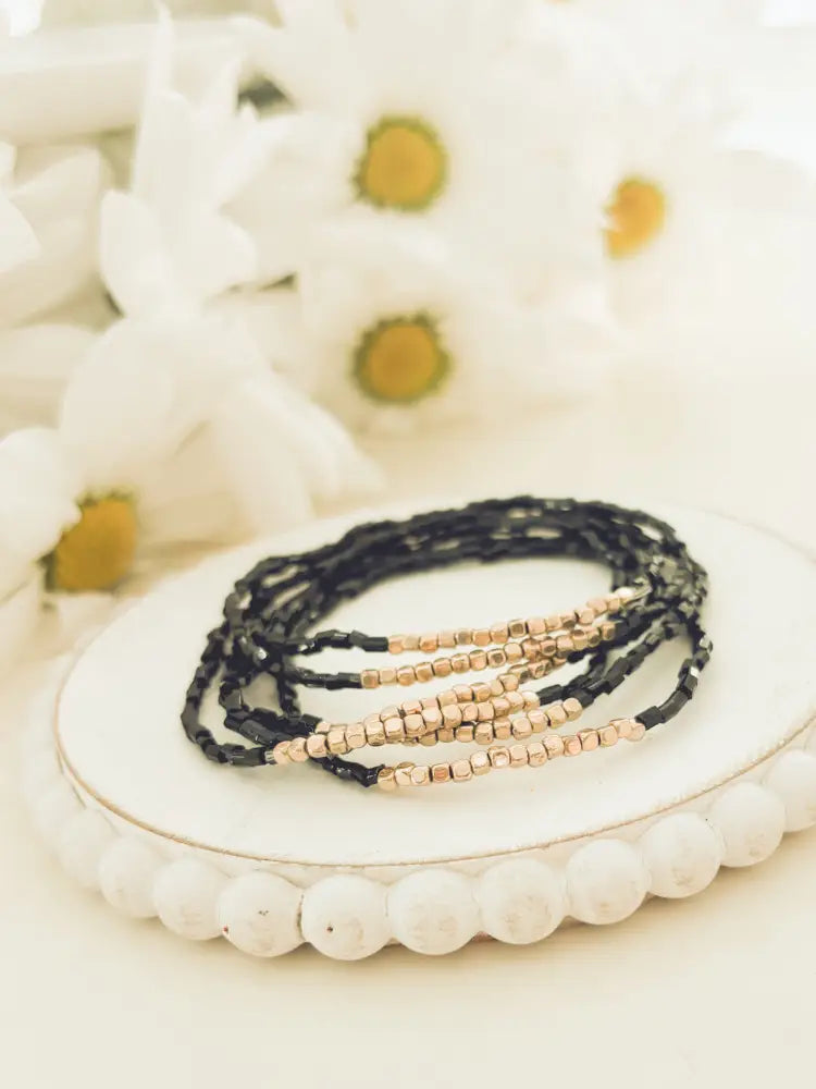 Elegant black and rose gold layered beaded stretch bracelet set arranged in a stack on a white decorative plate