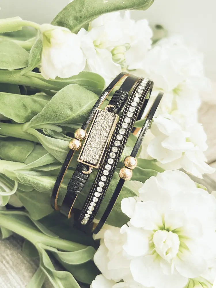 Black leather multi strand bracelet with gold accents and a rectangular crystal embellished plate with beads