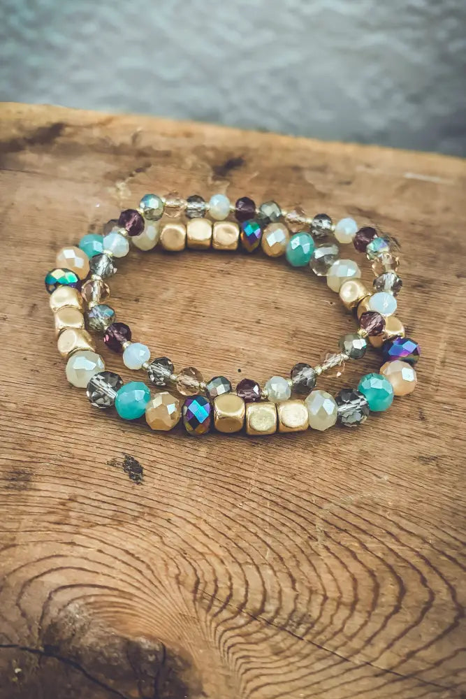 A pair of bohemian earth tone iridescent beaded stretch bracelets with gold-toned teal purple and clear crystal beads
