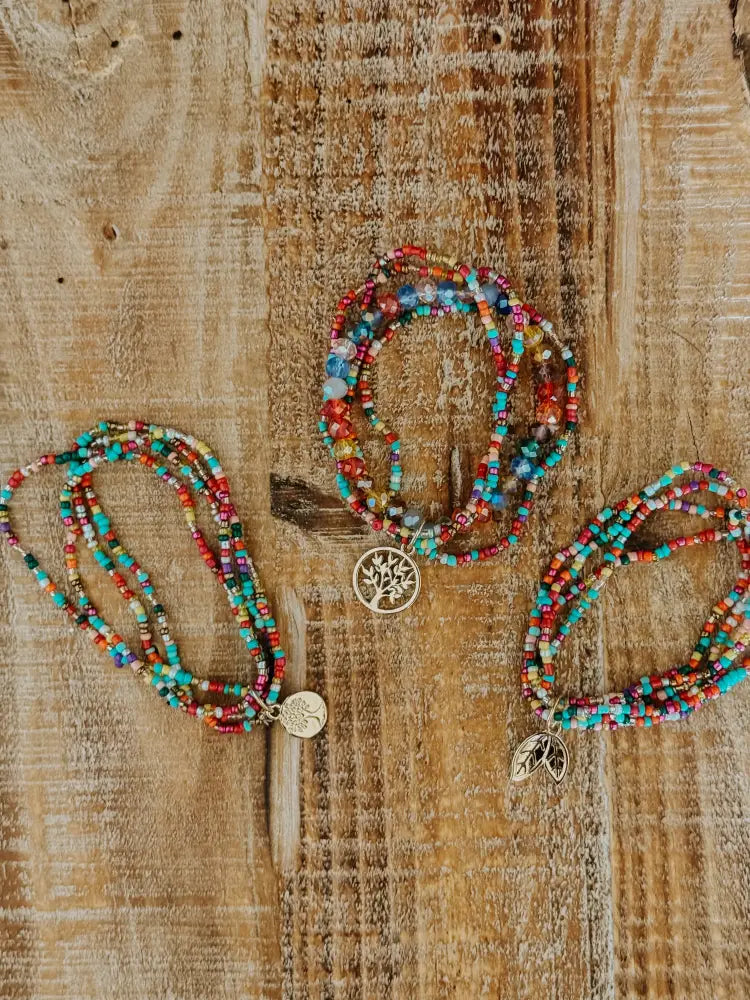Three colorful beaded stretch bracelets with metallic tree of life charms featuring red turquoise and multicolored beads