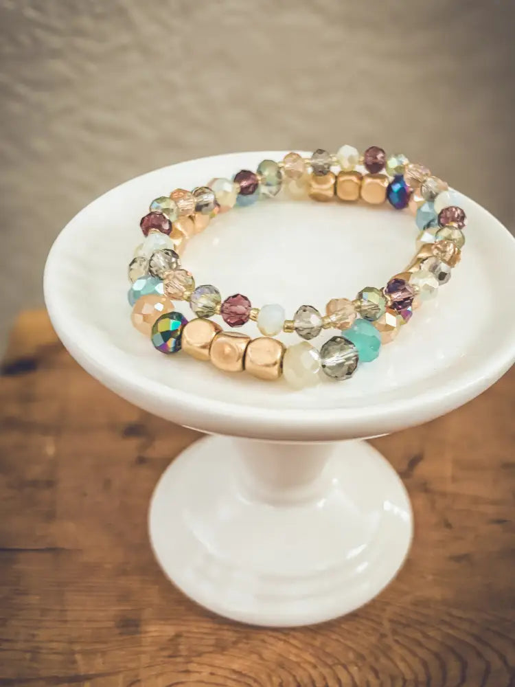 A delicate double-strand bohemian earth tone beaded stacking bracelet with iridescent gold blue purple teal and clear crystals
