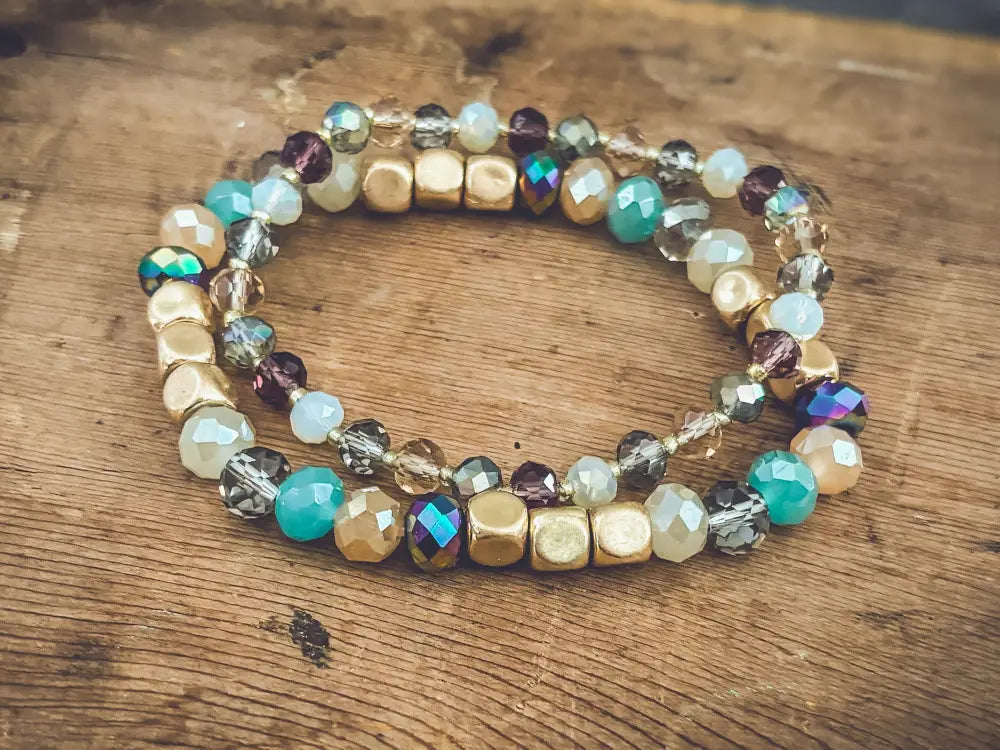 A pair of bohemian earth tone iridescent beaded stretch bracelets with faceted gold teal and geometric beads