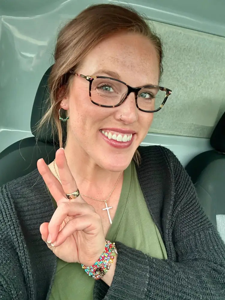 A woman wearing tortoiseshell-framed glasses with metallic accent modeling a tree of life colorful glass bead bracelet set
