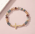 A delicate gold textured cross bracelet with multicolored faceted beads on a stretchy band