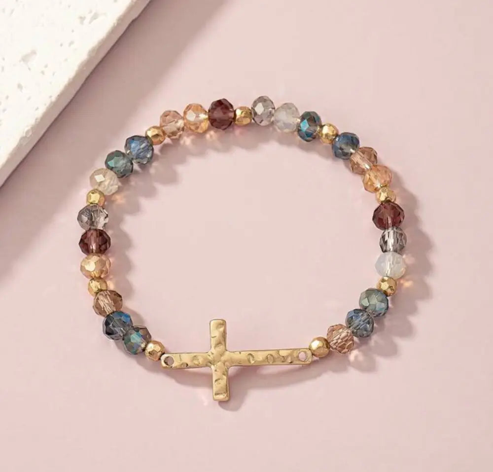 A delicate gold textured cross bracelet with multicolored faceted beads on a stretchy band