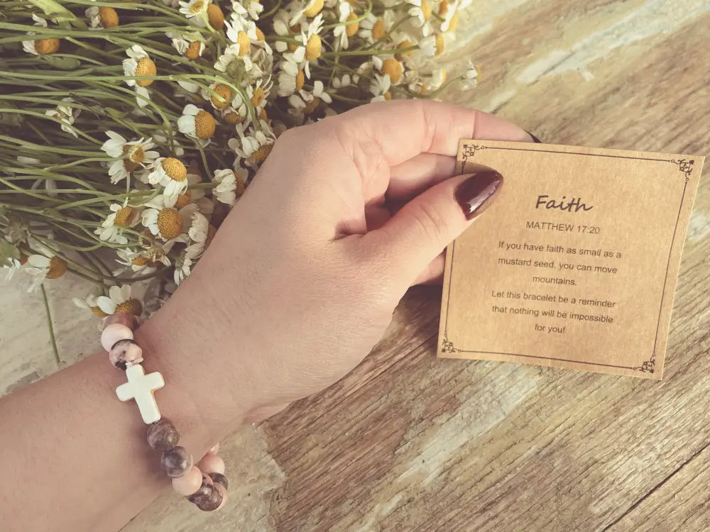 A pink and gray marbled cross stone stacking bracelet with white cross and speckled pink beads worn on a wrist