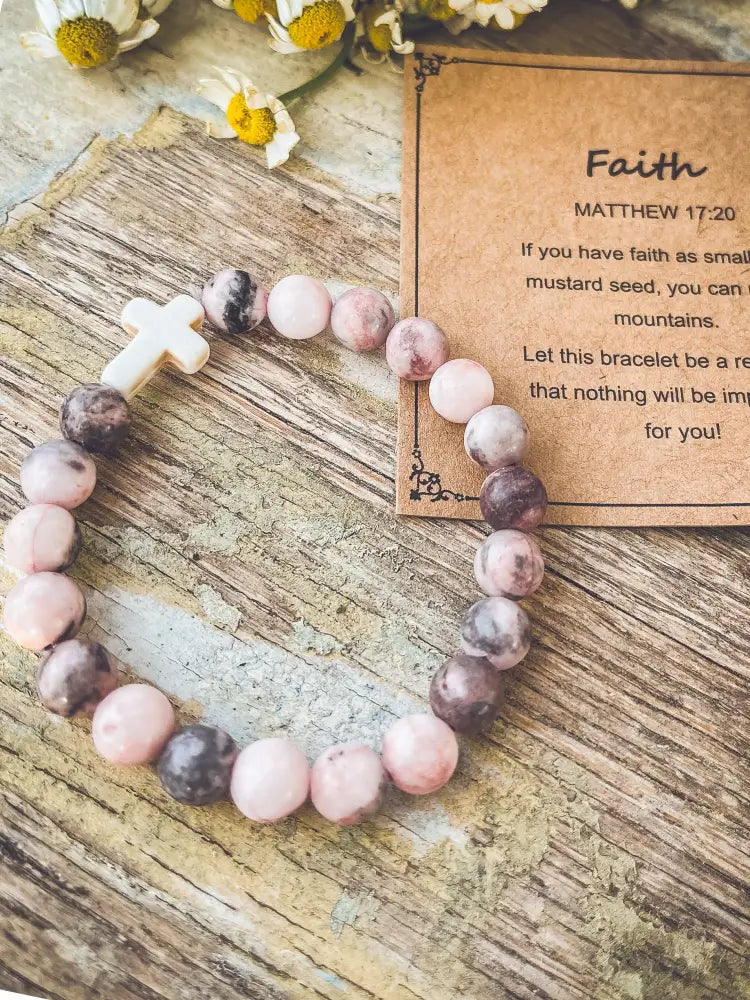 A delicate pink and gray marbled stone stacking bracelet with a white cross accent beside a faith card
