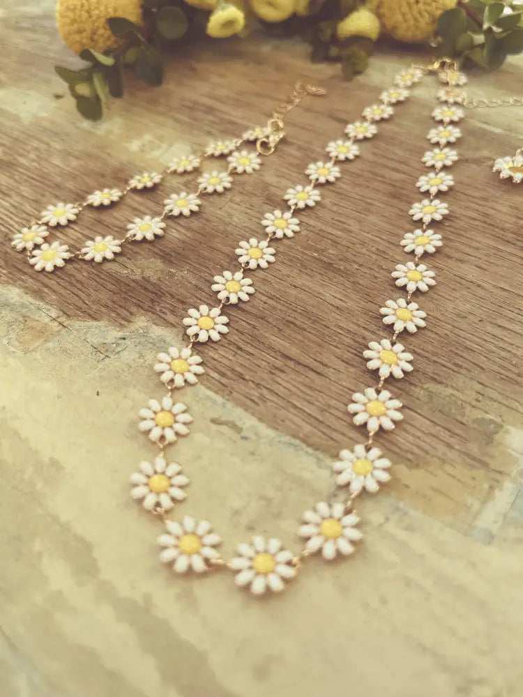 Delicate gold daisy enamel necklace featuring small white charms with yellow centers in a jewelry set