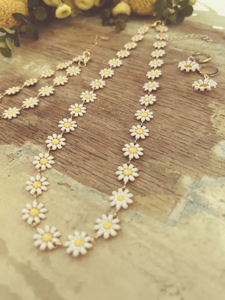 Gold daisy enamel necklace and earrings set featuring delicate gold-toned metal with white enamel petals and yellow centers