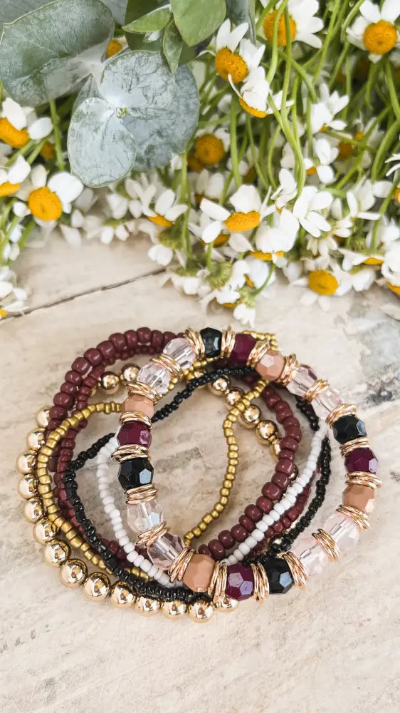 A set of five gold and burgundy earthy beaded stretch bracelets with maroon black white beads and clear crystal accents