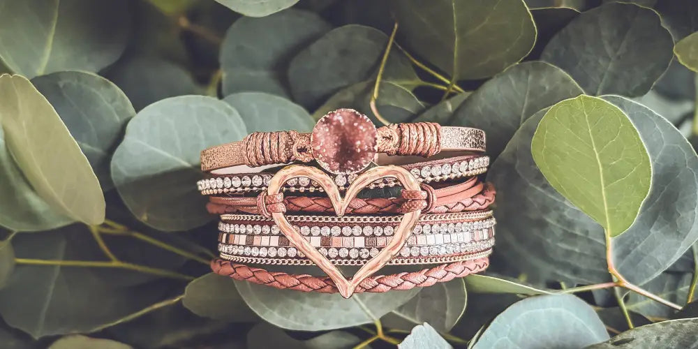 Rose gold braided leather heart charm bracelet featuring a central pink gemstone and intricate crystal details